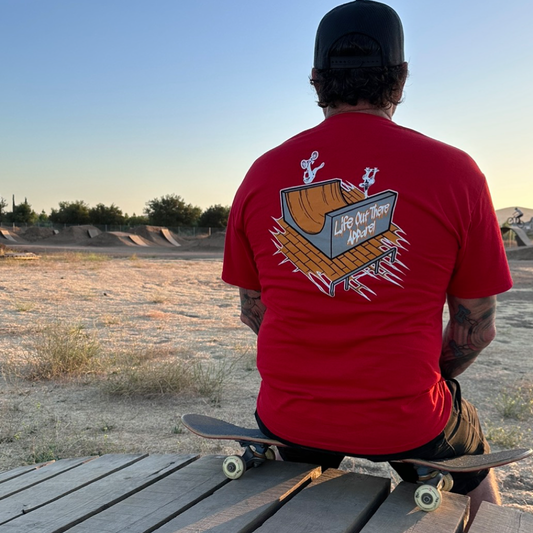 Life Out There Apparel “Fun is Not a Crime” Red Unisex tee shirt has a skateboarder and bmx rider having fun on a half pipe skateboard ramp. This picture has a man sitting on a skateboard. 