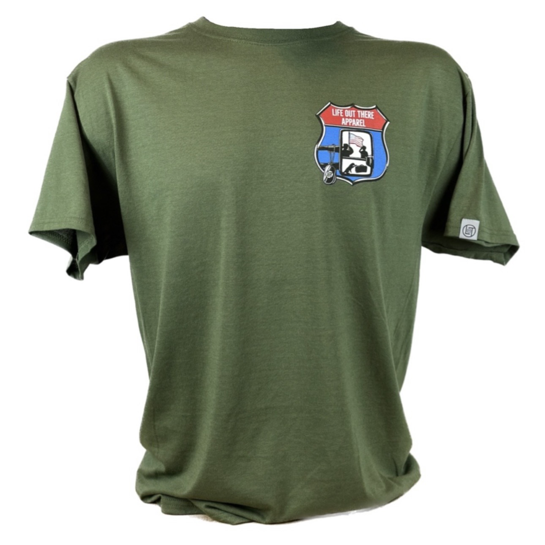 Military Green Unisex tee shirt from Life Out There Apparel “Leave It Behind” The design has a truck side mirror with the reflection of a male, female & K9 soldiers saluting the American flag (inside of an interstate sign) - bringing awareness to P. T. S. D. (post traumatic stress disorder) This photo of the front of the shirt with a white transparent background. 