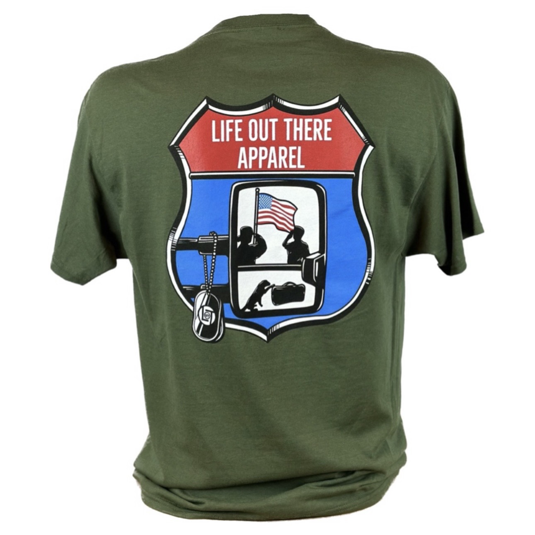 Military Green Unisex tee shirt from Life Out There Apparel “Leave It Behind” The design has a truck side mirror with the reflection of a male, female & K9 soldiers saluting the American flag (inside of an interstate sign) - bringing awareness to P. T. S. D. (post traumatic stress disorder) This photo of the back of the shirt with a white background. 
