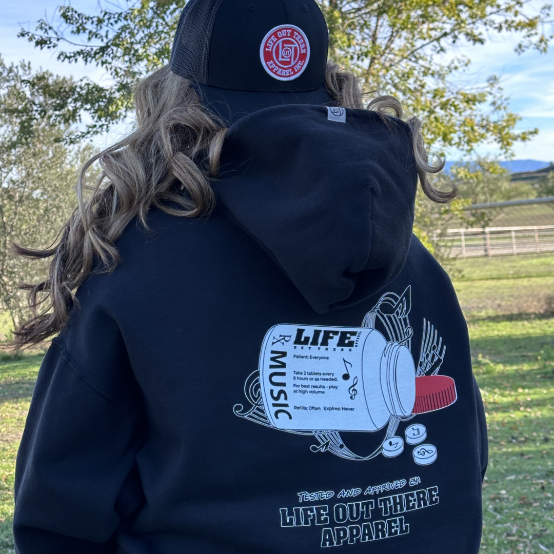 Life Out There Apparel “Music Is Medicine “ The Black Unisex Pullover Hoodie design is a medicine pill bottle tipped over with pills that have fallen out, that have music notes on them. This photo has a girl wearing headphones showing the back of the hoodie. 