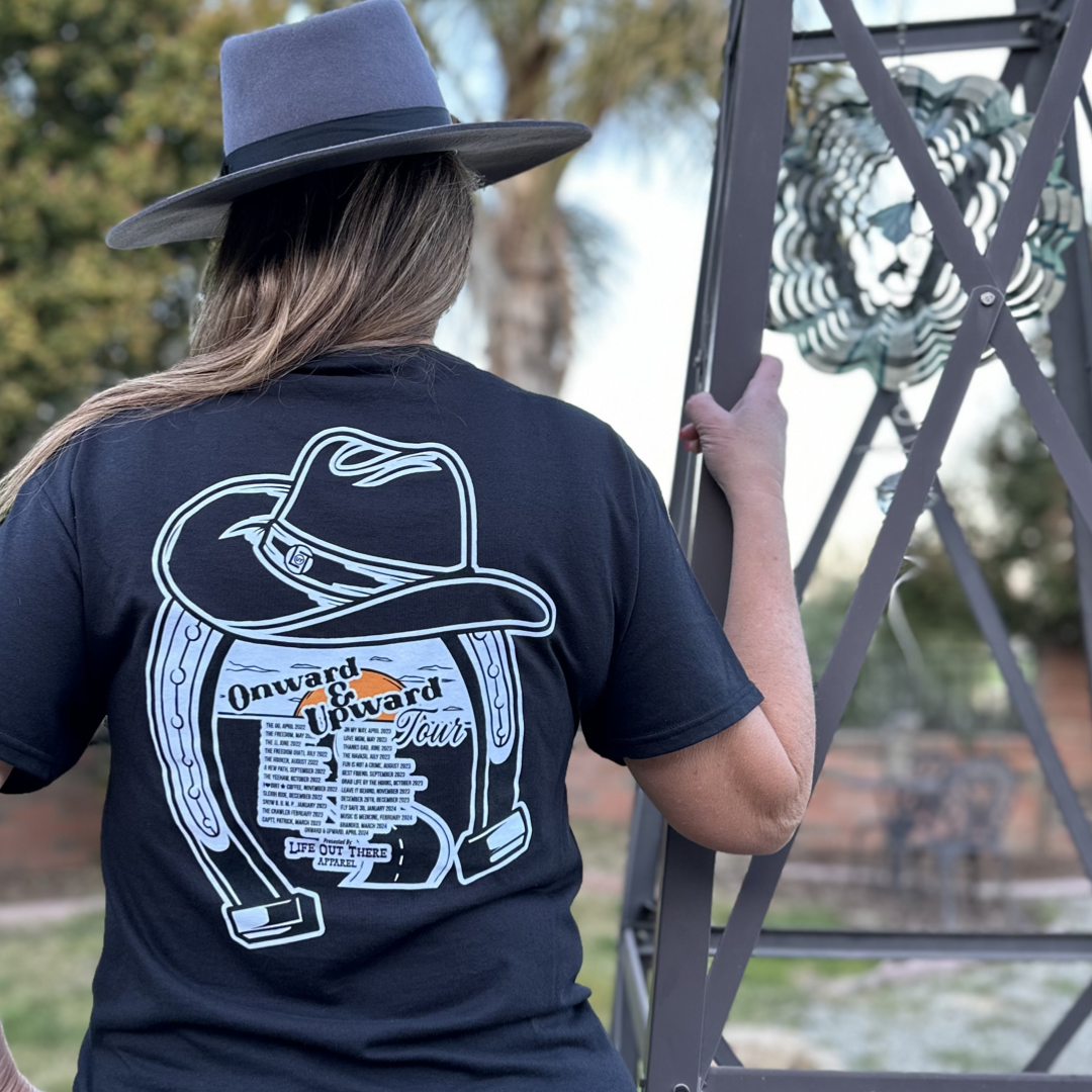 “ONWARD & UPWARD” Tour :
Life Out There Apparel “ONWARD & UPWARD” Tour Black Unisex tee is a country concert design with a cowboy hat & horseshoe on the front and back, with all the design names from the past 2 years (instead of city & tours dates) this photo is of a woman rocking a cowgirl hat standing next to a big windmill. 