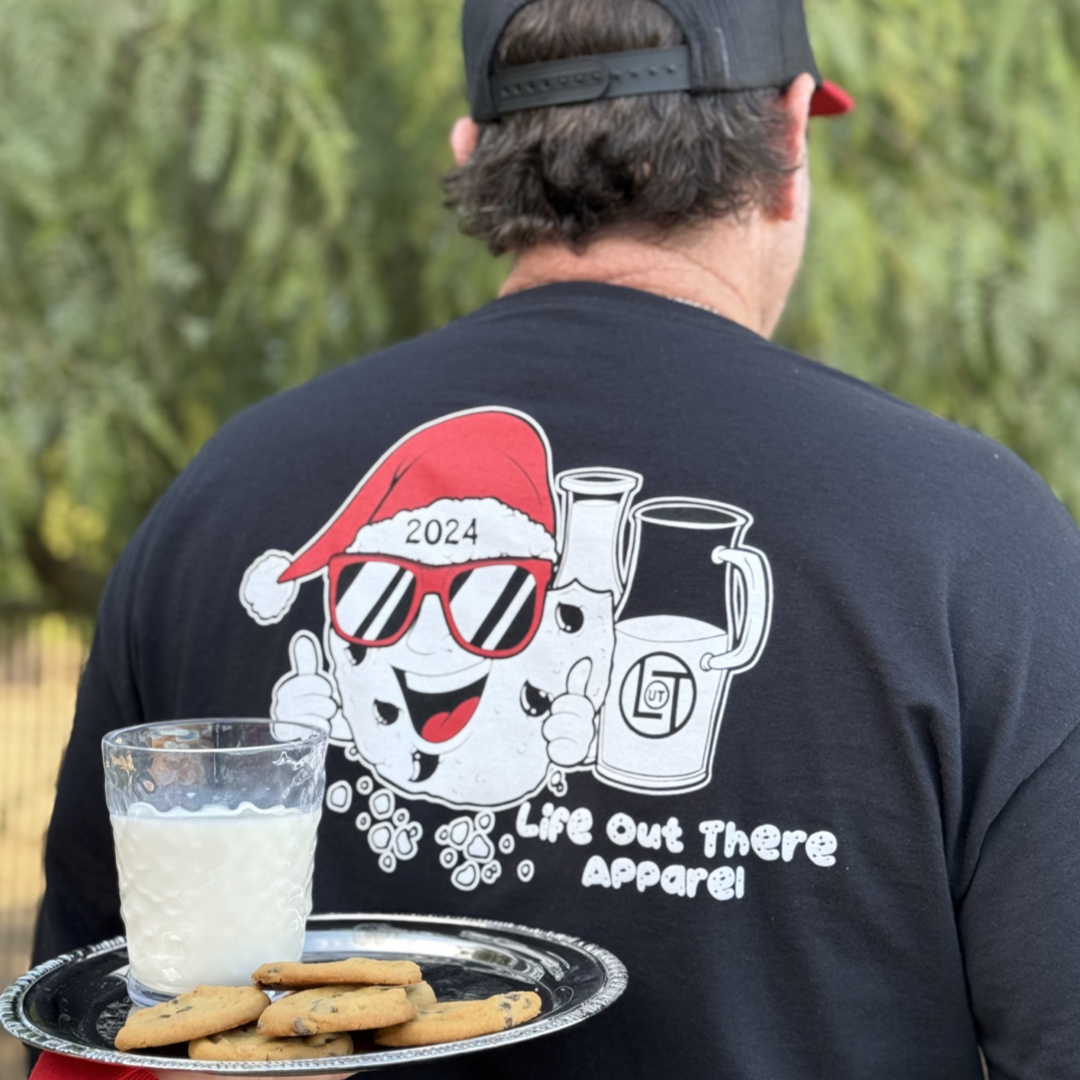 Black shirt with a cartoon cookie wearing a Santa hat and sunglasses labeled "2024," alongside glass milk cartons. Text reads, "Life Out The Apparel.