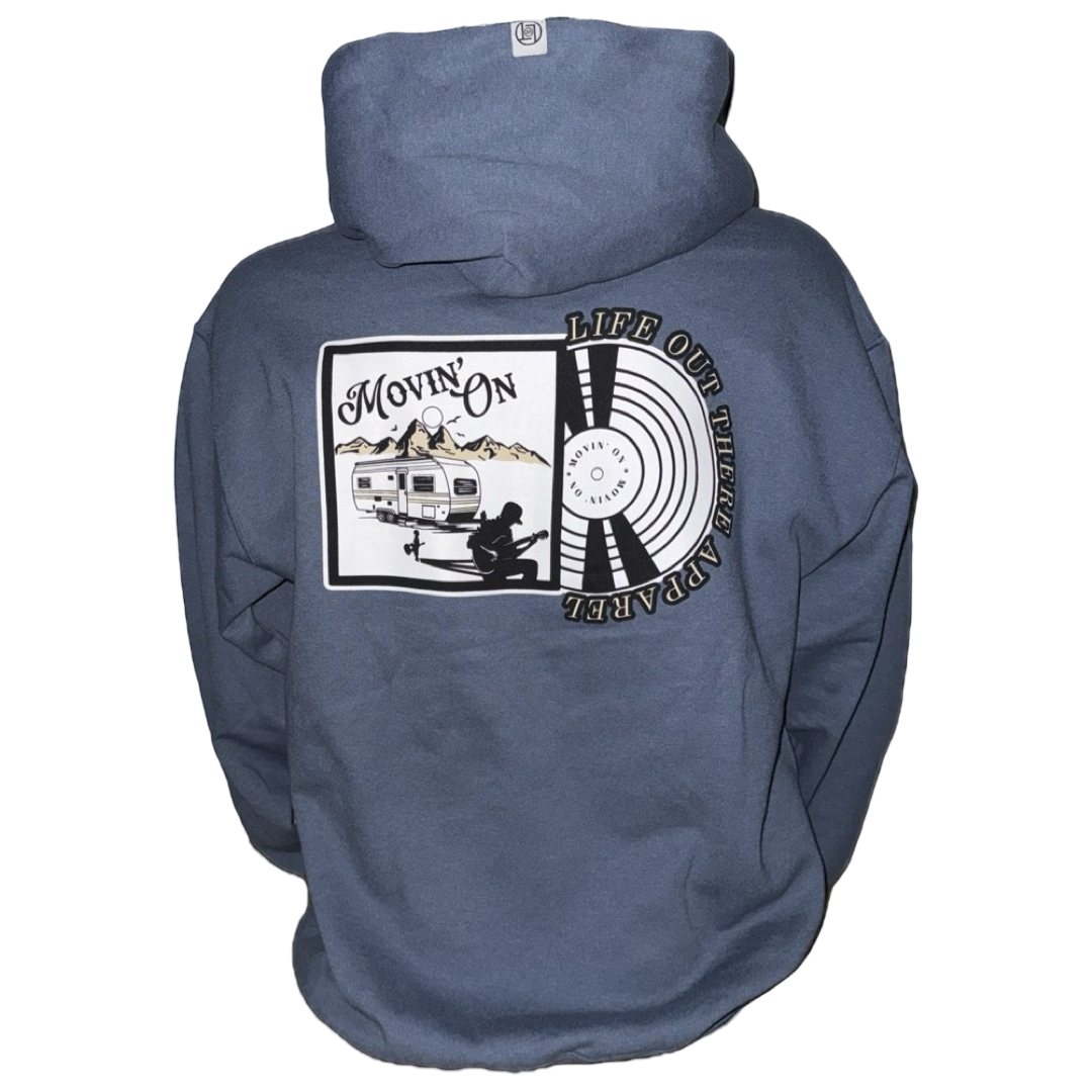 The Unisex Movin On Hoodie in Denim Blue by Life Out There Apparel showcases a back graphic of a camper, mountains, and guitarist, with a circular MOVIN ON design inspired by Jeremiah Watsons adventurous spirit.
