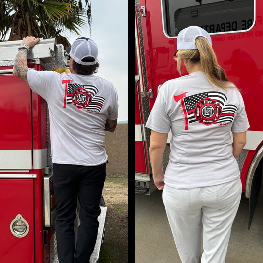 Two people in firefighter gear stand by fire trucks, wearing Life Out There Apparel’s Unisex Back The Red Tee in Silver. Their shirts display an American flag and Fire Rescue 119 logo, proudly honoring American firefighters.