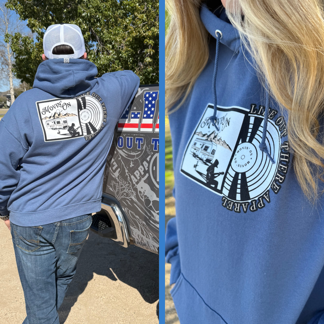 Wearing a Unisex - Movin On Hoodie in Denim Blue by Life Out There Apparel, someone leans on a decorated truck; a close-up highlights the vinyl record design with guitar player and trailer silhouettes.
