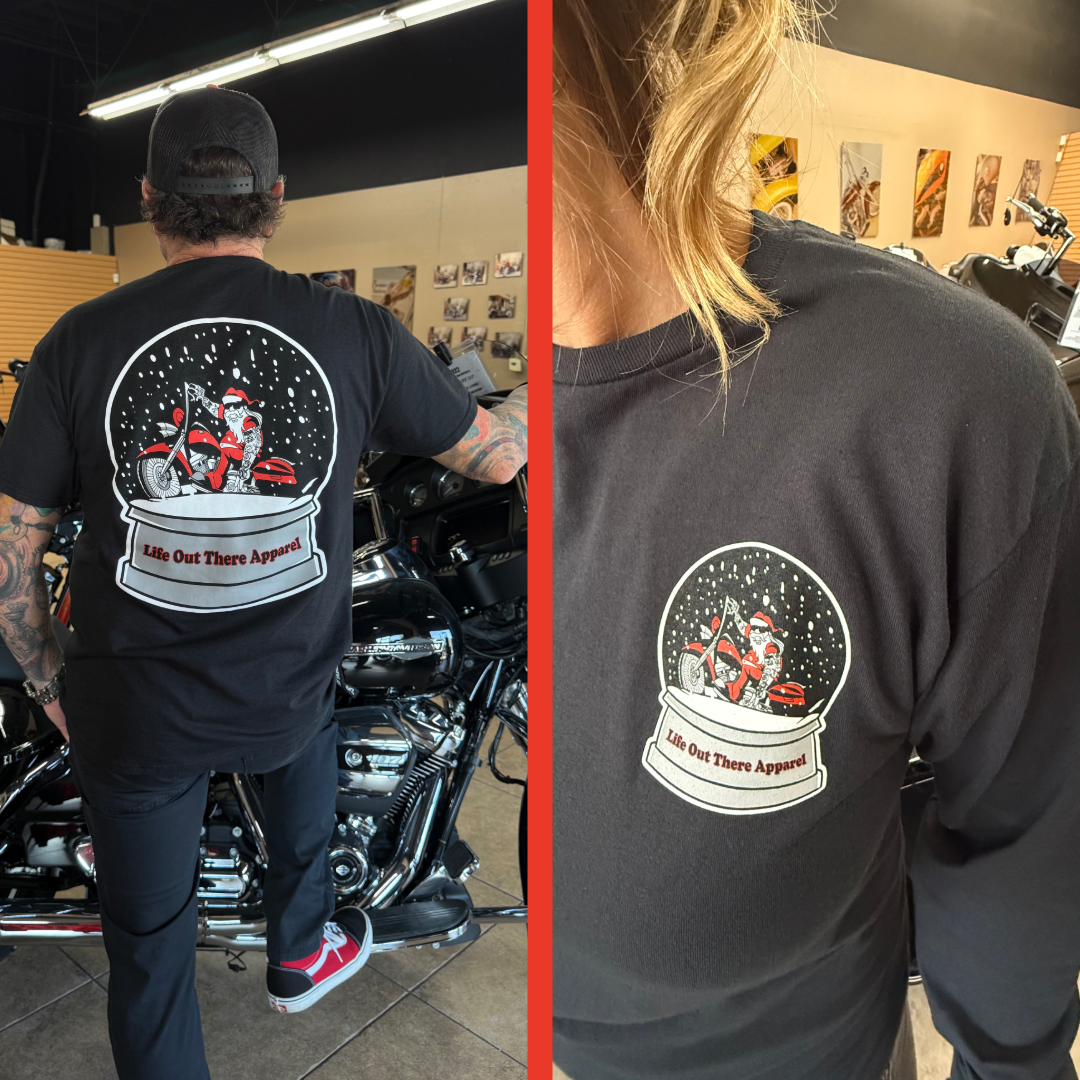 A person wears the Unisex - Dashing Through The Snow Tee in black by Life Out There Apparel, featuring a snow globe with Santa on a motorcycle, “Life Out There Apparel” text, and back and chest details surrounded by motorcycles.