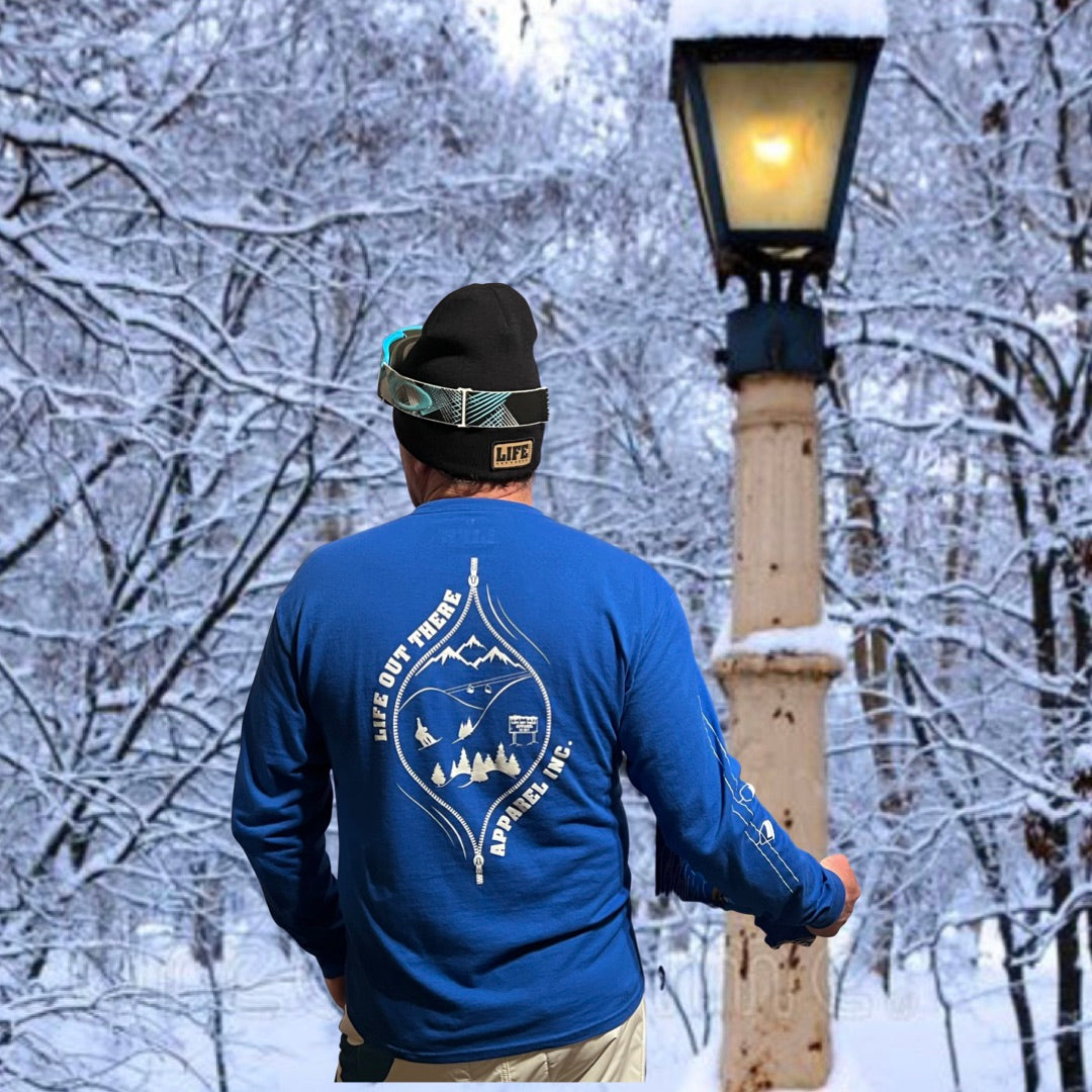 The Royal Blue Life Out There Apparel “Snow B. U. M. P. “ Unisex  long sleeve tee has a snowboard mountian scene design coming out of an unzipped zipper on the back of the shirt & a chair lift going down the right sleeve. Here is a man and a woman showing the back of the shirt while holding snowboards. 