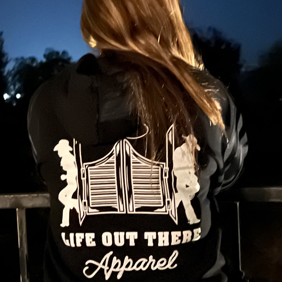 A model showcasing the black zip-up hoodie from Life Out there, featuring designs inspired by country music on the backside.